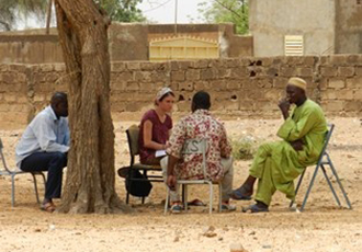 group of people sitting outside under a tree on fold up chairs