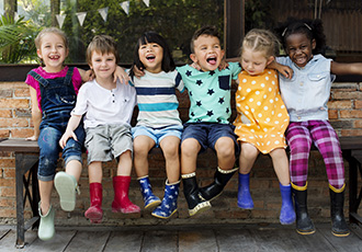 group of toddlers sitting with their arms around each other on a bench while smiling and laughing